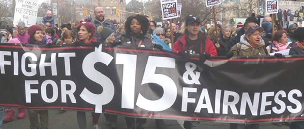Photo of people marching in the street holding a Fight for $15 & fairness banner