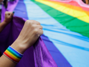 People at gay pride parade hold up a giant rainbow flag