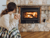 Women in beige sweater holding a mug by the fireplace