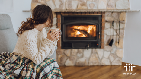 Women in beige sweater holding a mug by the fireplace