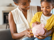 Black mother and daughter putting money in a piggy bank