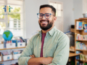 Teacher in his classroom with glasses looking at us with a smile. Looks like it was picture day.